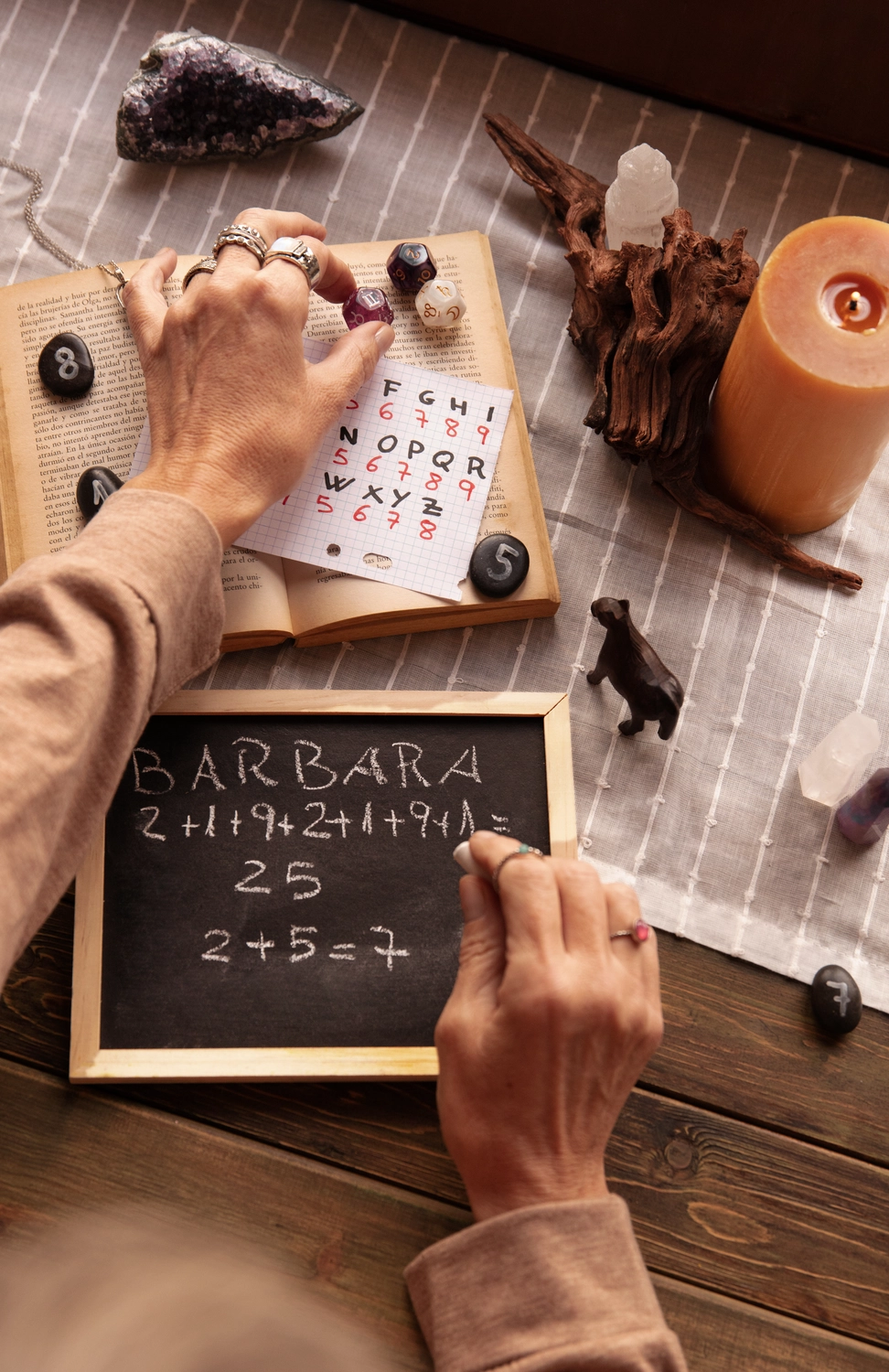 NumeroWunder - Numerologin und Thetahealing Praktikerin - Hände, die eine Namensanalyse auf eine kleine Tafel schreiben, neben einem Buchstabenraster und Kristallen.